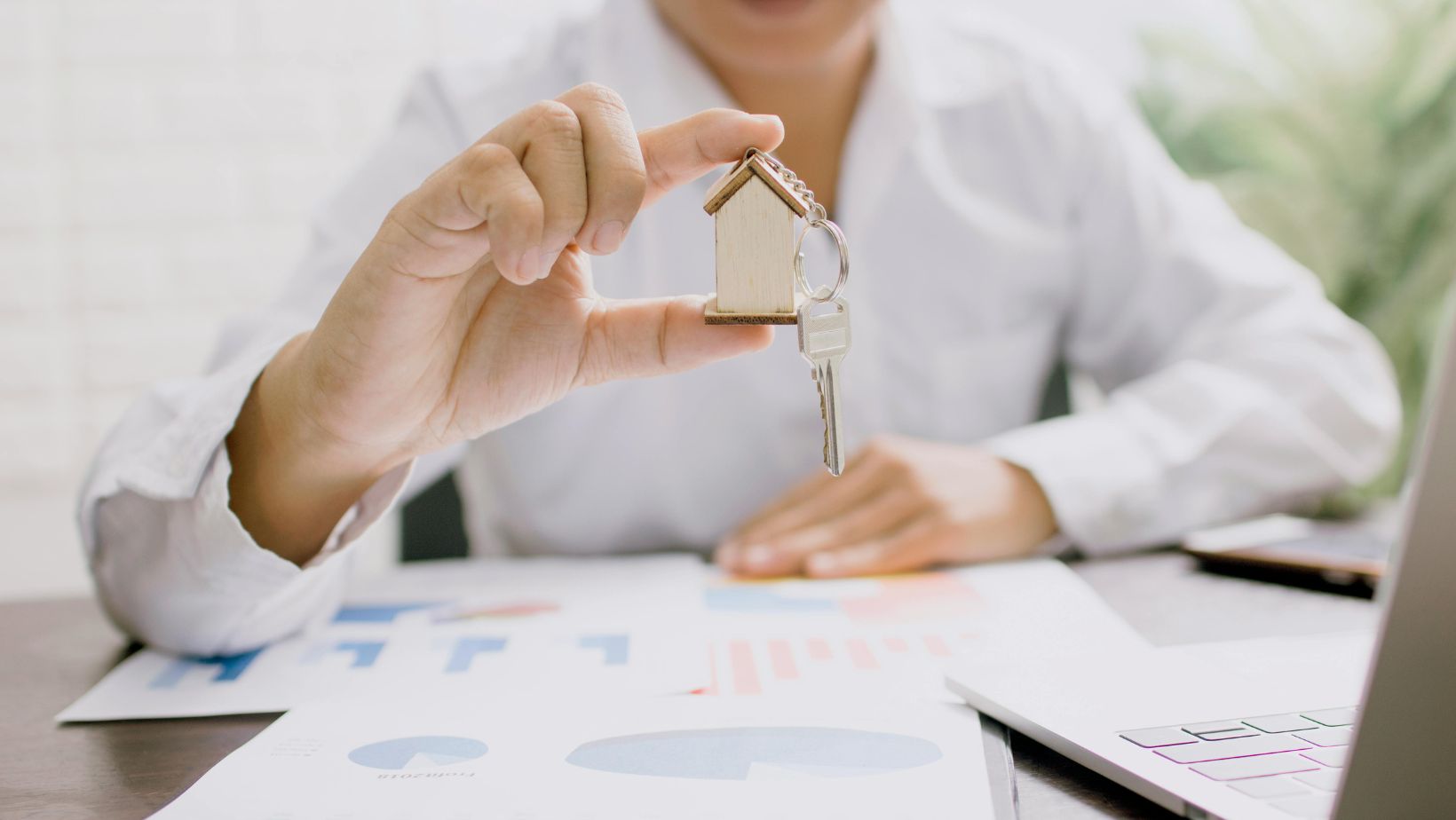 A person in a white shirt holding a small wooden model of a house with a key